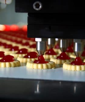 Automated machine dispensing red filling onto cookie bases in a production line. - Olive Oil Times