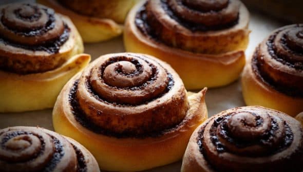 Freshly baked cinnamon rolls with a spiral design on a baking sheet. - Olive Oil Times