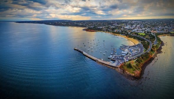 Aerial view of a coastal area featuring a harbor with boats and a shoreline. - Olive Oil Times