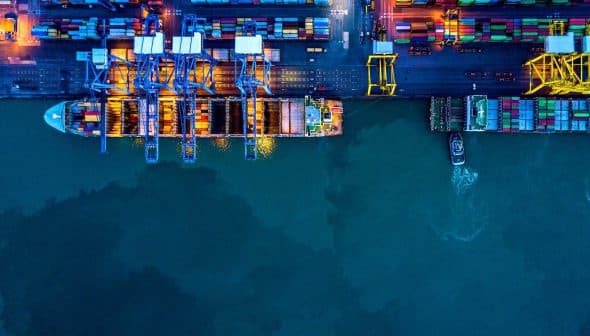 Aerial view of a container port with cranes and cargo containers at night. - Olive Oil Times