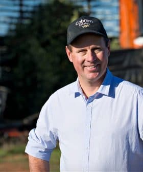 Man wearing a cap and a light shirt standing in front of agricultural machinery on a farm. - Olive Oil Times