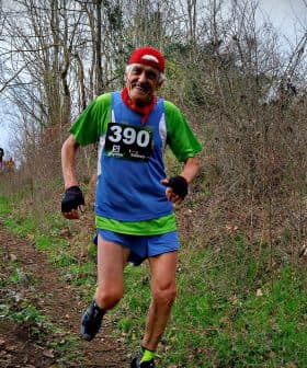 Two trail runners participating in a race on a wooded path, one wearing a green and blue outfit with a race number. - Olive Oil Times