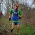 Two trail runners participating in a race on a wooded path, one wearing a green and blue outfit with a race number. - Olive Oil Times