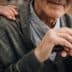 Close-up of an elderly man's hands resting on a cane, with a hand on his shoulder. - Olive Oil Times