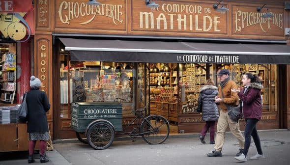 Shopfront of Le Comptoir de Mathilde featuring a chocolatier display and a bicycle cart. - Olive Oil Times