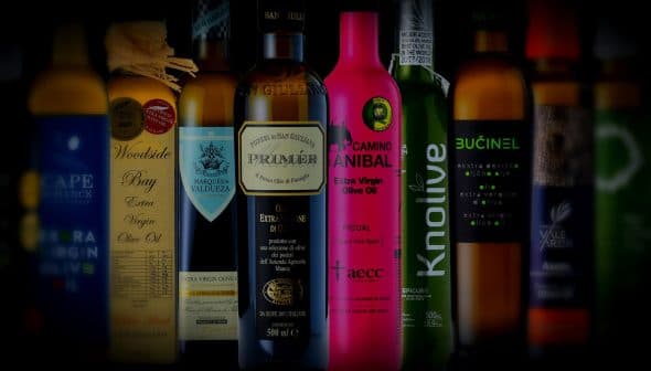 A collection of olive oil bottles featuring different brands and designs on a dark background. - Olive Oil Times