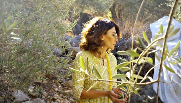 Woman with glasses standing among olive trees in a natural setting. - Olive Oil Times