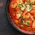 A black dish containing chicken pieces, red peppers, and herbs in a tomato-based sauce. - Olive Oil Times