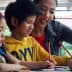A woman assisting two children with drawing activities at a table. - Olive Oil Times