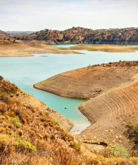 A view of a reservoir with a dry shoreline and surrounding hills in a natural landscape. - Olive Oil Times