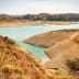 A view of a reservoir with a dry shoreline and surrounding hills in a natural landscape. - Olive Oil Times