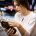 Woman inspecting a dark glass bottle of olive oil while shopping in a grocery store aisle. - Olive Oil Times