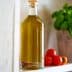 Glass bottle filled with olive oil placed on a shelf next to cherry tomatoes and a basil plant. - Olive Oil Times