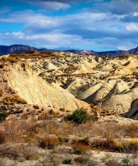 A desert landscape featuring rolling hills and distant mountains under a partly cloudy sky. - Olive Oil Times