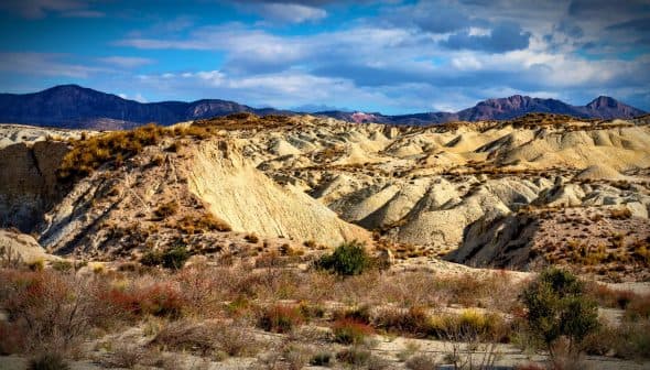 A desert landscape featuring rolling hills and distant mountains under a partly cloudy sky. - Olive Oil Times