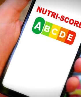 Hand holding a smartphone displaying the Nutri-Score logo with letters A to E in colored boxes. - Olive Oil Times