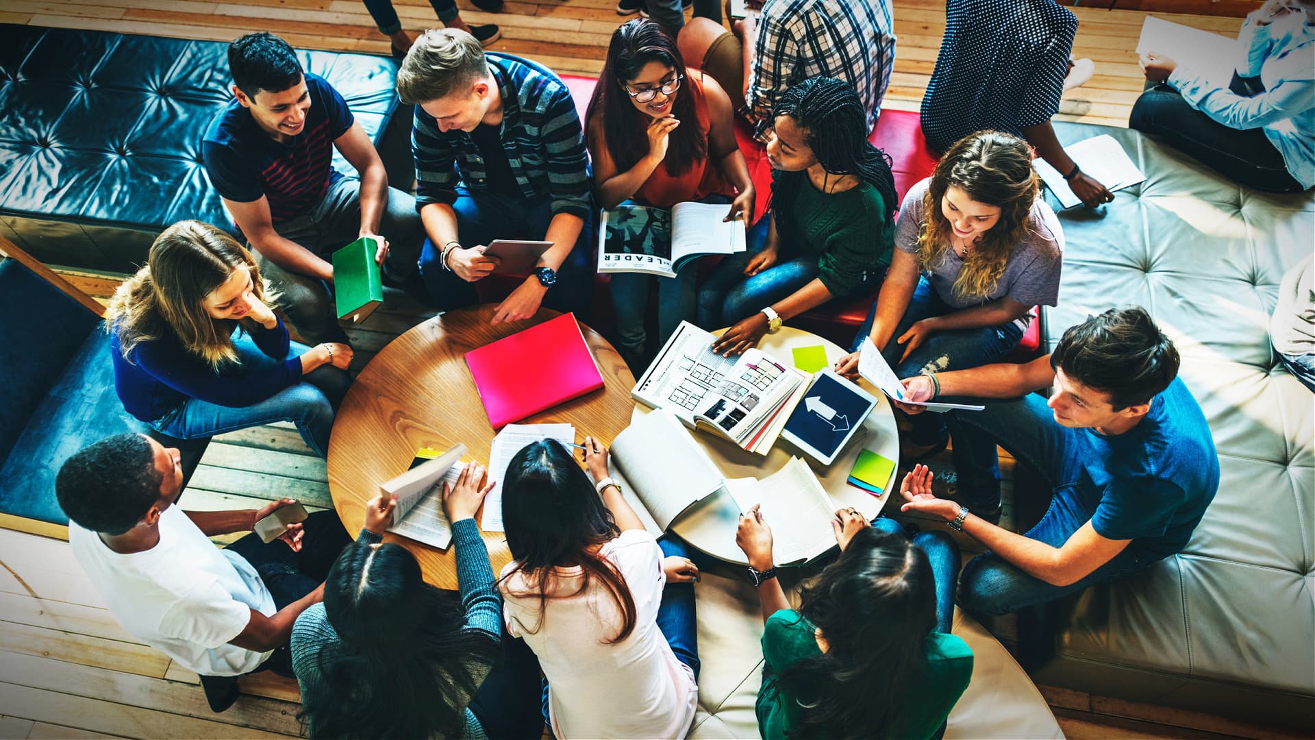 A diverse group of individuals gathered around a table, engaged in discussion with notebooks and materials. - Olive Oil Times