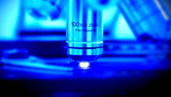 Close-up of a microscope objective lens labeled 100x with a blue background. - Olive Oil Times