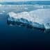 A large glacier edge with icebergs floating in calm water under a clear sky. - Olive Oil Times
