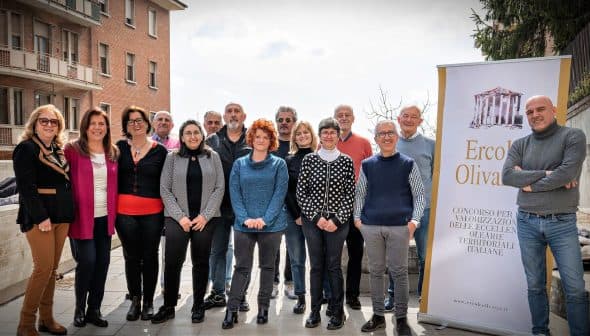 A group of individuals standing together for a photo, with a banner in the background featuring the text 'Ercole Olivario'. - Olive Oil Times