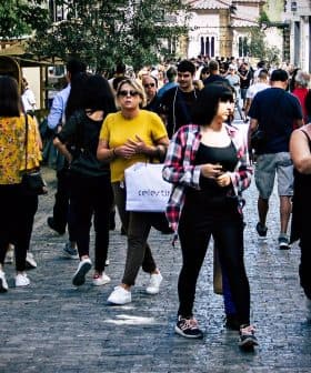 Group of people walking on a cobblestone street in an urban area with shops and trees. - Olive Oil Times
