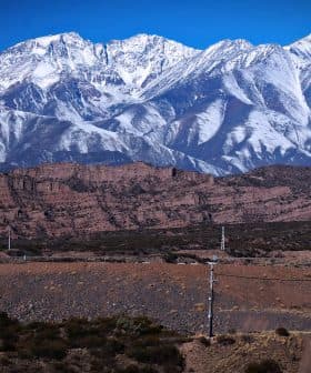 A view of snow-capped mountains rising above rocky terrain under a clear blue sky. - Olive Oil Times