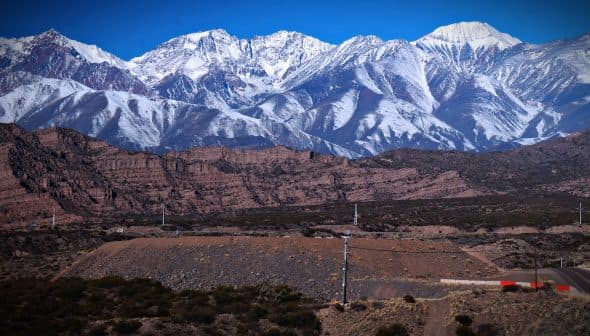 A view of snow-capped mountains rising above rocky terrain under a clear blue sky. - Olive Oil Times