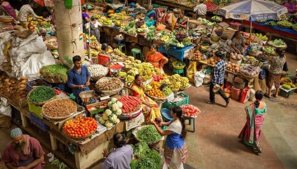 A vibrant market scene filled with various fresh fruits and vegetables on display at stalls. - Olive Oil Times