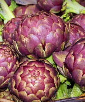 A basket filled with fresh purple artichokes, showcasing their rounded shape and green leaves. - Olive Oil Times