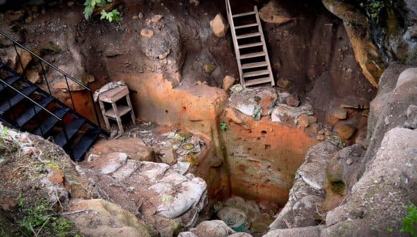 Excavated pit showing a wooden ladder and stone walls with visible earth and rocks. - Olive Oil Times