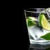 A glass filled with water, ice cubes, and lime wedges against a black background. - Olive Oil Times
