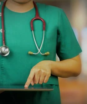 Healthcare professional in green scrubs using a tablet device while wearing a stethoscope. - Olive Oil Times