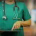 Healthcare professional in green scrubs using a tablet device while wearing a stethoscope. - Olive Oil Times