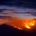 A mountain landscape with a wildfire burning along the slope under a twilight sky. - Olive Oil Times