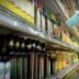 A person reaching for a bottle of olive oil on a grocery store shelf filled with various oils. - Olive Oil Times