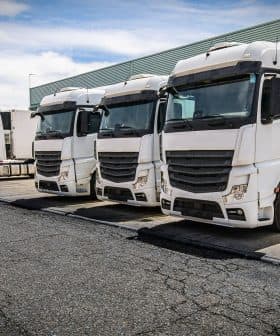 Four white delivery trucks parked in a row at a loading dock area. - Olive Oil Times