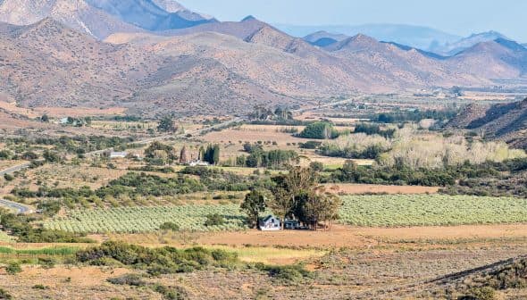 A rural landscape featuring fields, a house, and mountains in the background. - Olive Oil Times