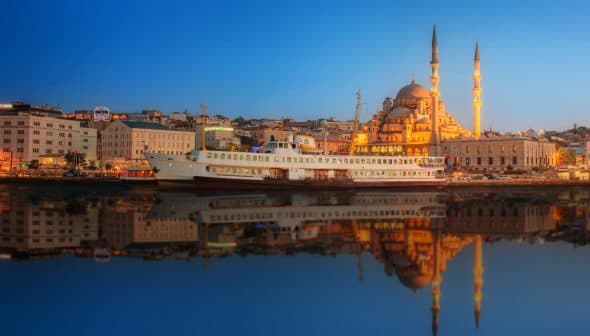 A ferry docked near a mosque in Istanbul during sunset with reflections on the water. - Olive Oil Times