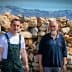 Two men posing in front of a stone wall with mountains in the background. - Olive Oil Times