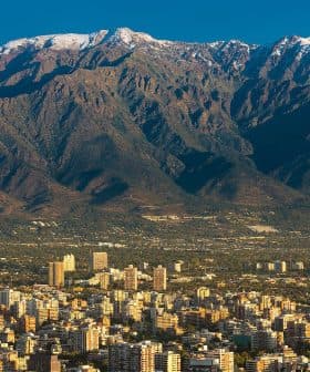 A mountain range with snow-capped peaks in the background and a cityscape in the foreground. - Olive Oil Times