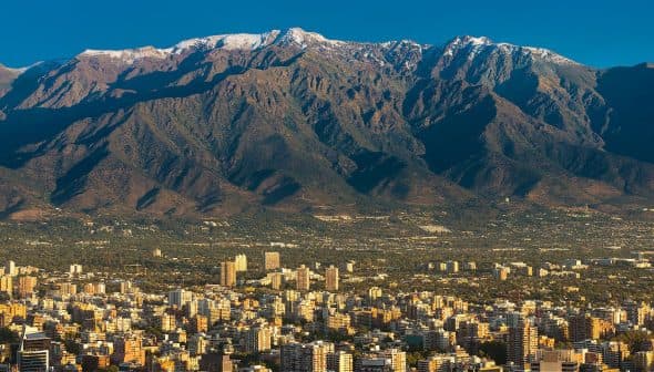 A mountain range with snow-capped peaks in the background and a cityscape in the foreground. - Olive Oil Times
