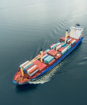 Aerial view of a container ship carrying colorful cargo containers on calm water. - Olive Oil Times