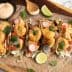 Five shrimp tacos topped with vegetables and sauce on a wooden serving board. - Olive Oil Times