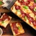 A rectangular pepperoni pizza topped with tomato sauce and fresh basil leaves, served in a baking tray. - Olive Oil Times
