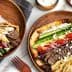 A pita wrap filled with beef, vegetables, and fries next to a plate of gyro with toppings. - Olive Oil Times