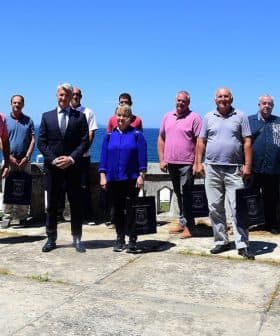 A group of individuals standing together outdoors with a clear blue sky in the background. - Olive Oil Times