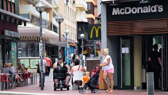 A street scene featuring a McDonald's restaurant and pedestrians, including a woman with a stroller and a man on a mobility scooter. - Olive Oil Times
