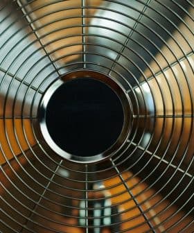 Close-up view of a metal oscillating fan with a wire grille and circular center. - Olive Oil Times