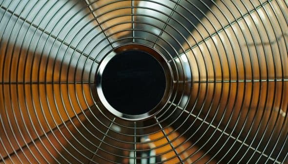 Close-up view of a metal oscillating fan with a wire grille and circular center. - Olive Oil Times