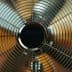 Close-up view of a metal oscillating fan with a wire grille and circular center. - Olive Oil Times